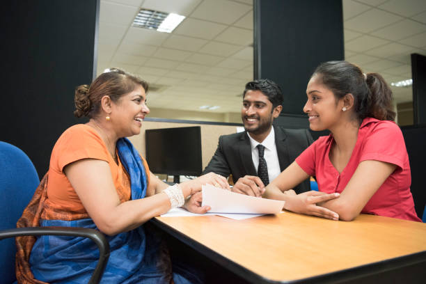 Financial adviser in meeting with young couple Mature woman in finance advice meeting with young man and woman and discussing documents, they are sitting at the table with cheerful expressions sri lanka women stock pictures, royalty-free photos & images