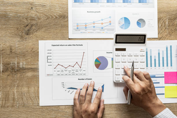 Financial scholars are pressing white calculators to calculate numbers on financial documents to verify the accuracy of company financial data line and pie chart documents. Finance concept. stock photo