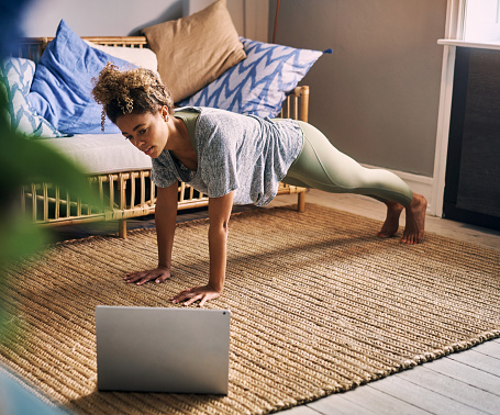 Shot of a sporty young woman using a laptop while exercising at home