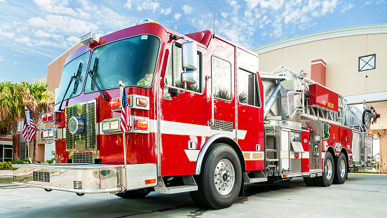 A hook and ladder fire engine truck sits in front of the fire engine house.