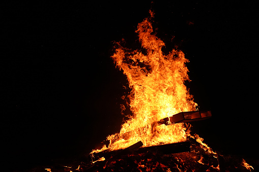 Pallets being used as fuel for a large bonfire and as an added bonus it appears  to have  fire demon in the flames. I see a figure with a Skelton-like face and arms out stretched at the top of the fire facing the right.