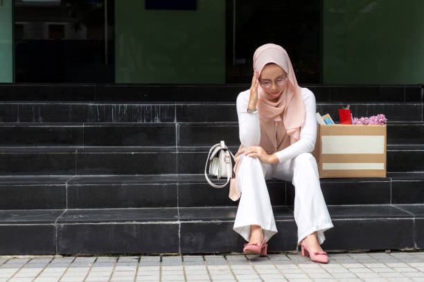 fired muslim businesswoman sitting outside office with her belongings unhappy Asian woman wearing hijab, feeling upset, sitting on staircase with her box of belongings after getting fired from her job insolvente stock pictures, royalty-free photos & images