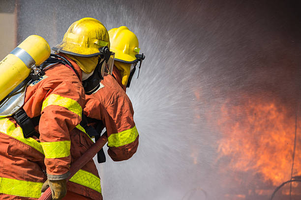 2 firefighters spraying water in fire fighting operation stock photo