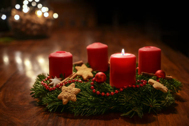 First Advent - decorated Advent wreath from fir branches with red burning candles on a wooden table in the time before Christmas, festive bokeh in the warm dark background, copy space, selected focus stock photo