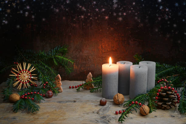 First Advent, one of four candles is lighted, Christmas decoration like nuts, straw star, cones and fir branches on rustic wood against a dark brown background, copy space stock photo
