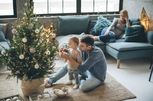 First Christmas as a family Family with one child decorating Christmas tree. They are happy and enjoy in preparation for holidays. chrismas tree stock pictures, royalty-free photos & images