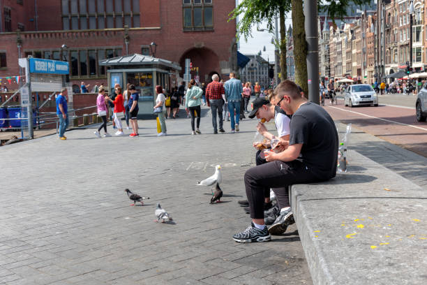 First sunny Sunday, less travel restrictions, already busy in the city centre om Amsterdam. Tourist eating fast food and birds begging for some too. Amsterdam, The Netherlands - July 4th 2021: First sunny Sunday, less travel restrictions, already busy in the city centre om Amsterdam. Tourist eating fast food and birds begging for some too. van Dijk stock pictures, royalty-free photos & images