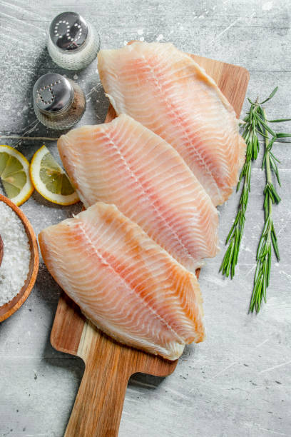 Fish fillet on a wooden cutting Board with rosemary, spices and lemon slices. stock photo