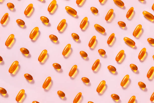Fish Oil Capsules Abundance of yellow fish oil capsules repetition on soft pink background fish oil stock pictures, royalty-free photos & images