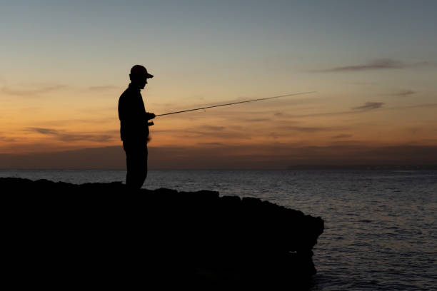 A fisherman with the rod at sunset against the light in Majorca, Spain stock photo