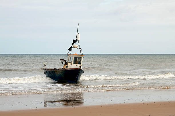 Fishing boat on the beach A working crab boat in the surf on Cromer beach, Norfolk. Cromer is world famous for its crabs. (Intentional high contrast.) crabbing stock pictures, royalty-free photos & images