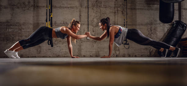 Fit And Strong Two young muscular girls doing plank exercise at the gym workout. cross training stock pictures, royalty-free photos & images