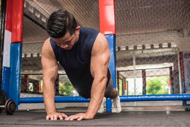 A fit asian man does diamond push ups at a MMA gym. Body weight calisthenics or HIIT workout. Training chest, abs and triceps. stock photo