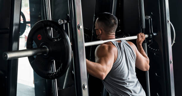 A fit asian man performs some squats at the smith machine. Working out, leg day training at the gym. stock photo