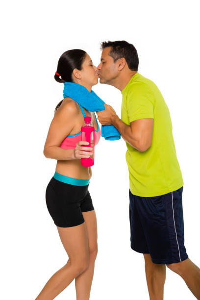 Fit Hispanic couple in workout attire kissing. Man kisses woman. Isolated on white background. stock photo