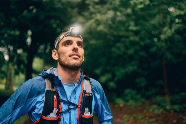 Fit male jogger with a headlamp rests during training for cross country trail race in nature park stock photo