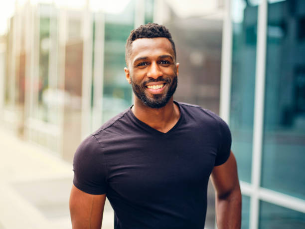 Fit Man Standing Outdoors in a City A fit black man with a beard, standing outdoors in a city area. handsome people stock pictures, royalty-free photos & images