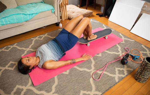 Fit woman doing pelvis thrusts on floor using a skateboard A fit tanned sporty woman is performing pelvic thrusts and using a skateboard under her feet for added balance and effect. pelvic floor stock pictures, royalty-free photos & images