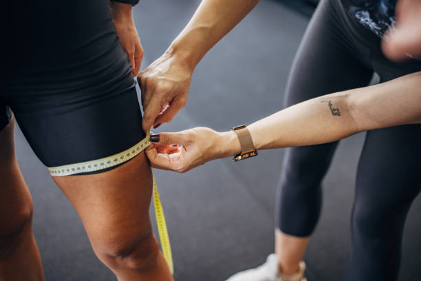 Fit woman measuring her thigh Two women, female personal trainer measuring her client's thigh in gym. Athletic stock pictures, royalty-free photos & images