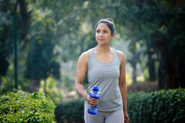 Fit woman with dumbbell shape water bottle at park Fit woman running in sportswear with dumbbell shape water bottle at park indian women walking stock pictures, royalty-free photos & images