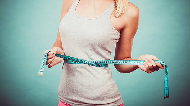 Fitness girl measuring her waistline Weight loss, slim body, healthy lifestyle concept. Fit fitness girl measuring her waistline with measure tape on blue dieting stock pictures, royalty-free photos & images