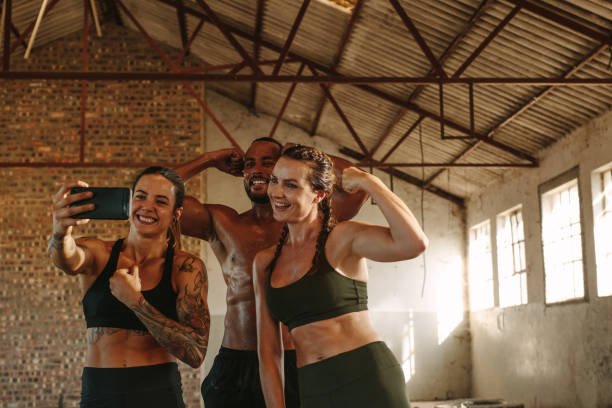 Fitness people taking selfie Woman taking a selfie with smart phone after workout session with friends. Group of three people taking self portrait inside abandoned warehouse. cross training stock pictures, royalty-free photos & images