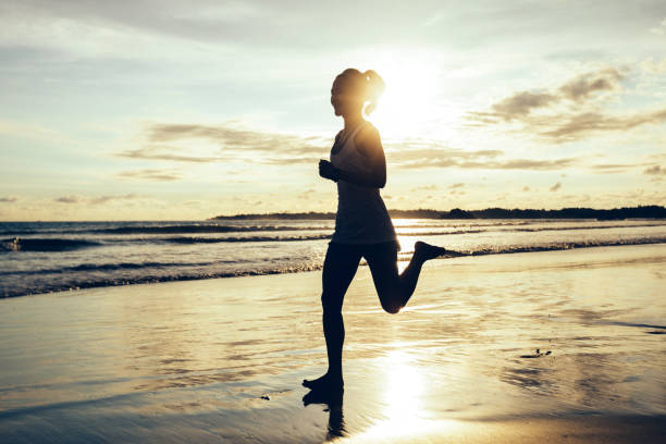 Fitness woman runner running on sunset beach stock photo