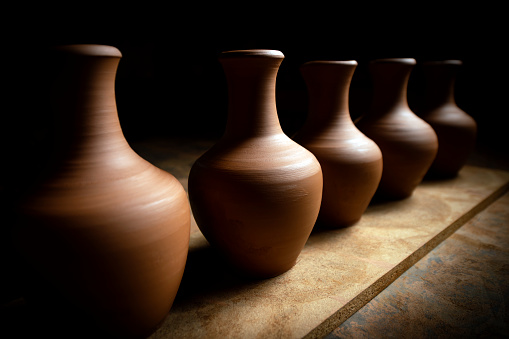 Five ceramic jugs are on the wooden board. The jugs standing diagonally receive lateral light at the same time.