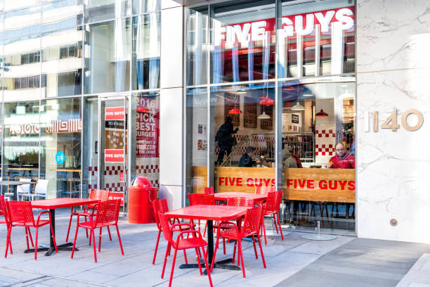 Five Guys restaurant, store burger chain entrance in District of Columbia with chairs, tables, outside, outdoor sitting area, people inside eating Washington DC, USA - March 9, 2018: Five Guys restaurant, store burger chain entrance in District of Columbia with chairs, tables, outside, outdoor sitting area, people inside eating five people stock pictures, royalty-free photos & images