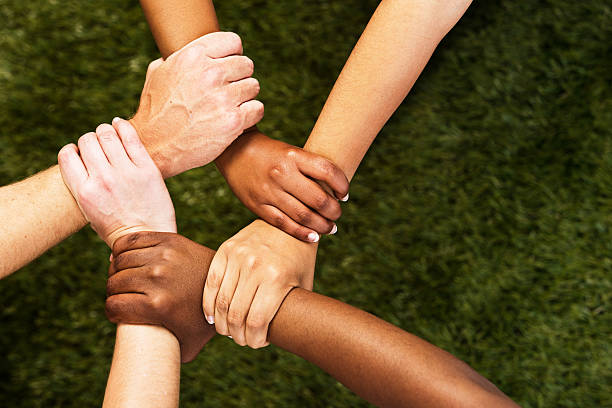 Five mixed hands clasped in unity against grass stock photo