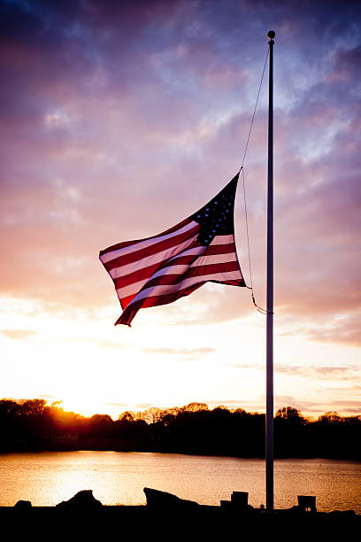 Flag at Half Mast Flag at half mast overlooking the water at sunset. flag at half staff stock pictures, royalty-free photos & images