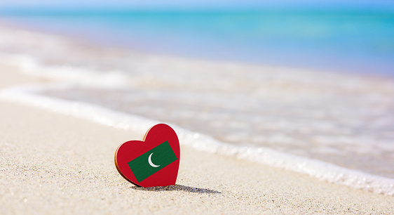 Flag of the Maldives in the shape of a heart on a sandy beach. The concept of the best vacation in Maldives resorts