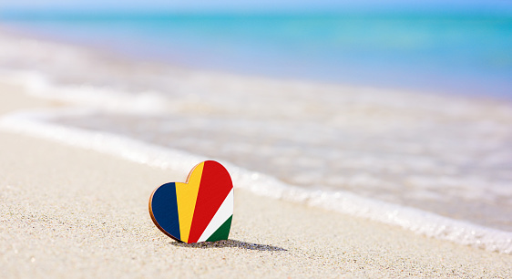 Flag of the Seychelles in the shape of a heart on a sandy beach. The concept of the best vacation in Seychelles