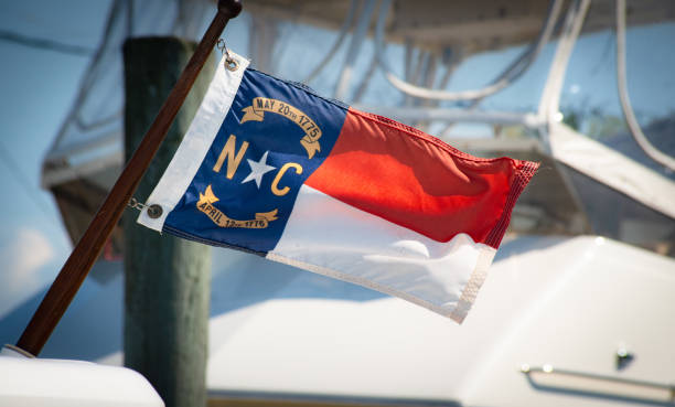 NC Flag A North Carolina flag waves in the wind, while a boat sits in the background. north carolina us state photos stock pictures, royalty-free photos & images