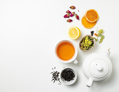 Flat lay a cup of black tea, fruit and herbal tea, with lemon and tea pot on a white background. The concept of a healthy drink. Top view and copy space.