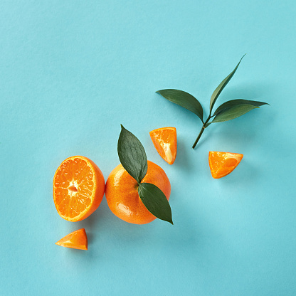 Top view of tropical exotic citrus fruits mandarine whole and slices with green leaves on a blue paper background