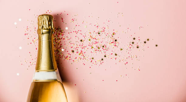 Flat lay of Celebration. Champagne bottle with sprinkles on pink background. stock photo
