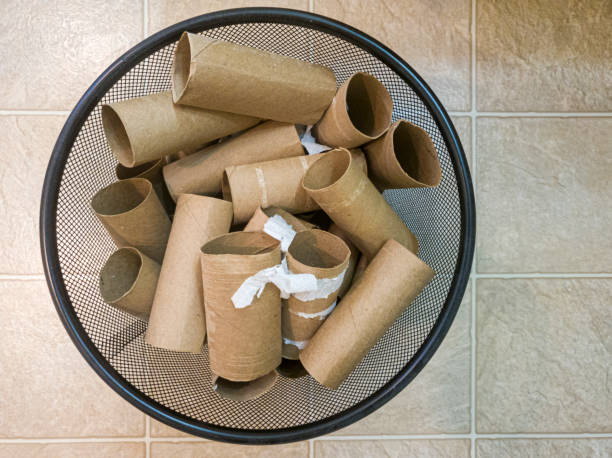 Flat lay top view image of a metal trash bin full of empty toilet paper rolls with some paper leftovers stuck on them. stock photo