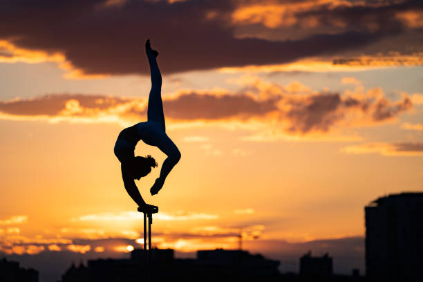 Flexible female circus Artist keep balance and doing contortion on the rooftop against dramatic sunset and cityscape. Motivation, passion and achievement concept Flexible female circus Artist keep balance and doing contortion on the rooftop against dramatic sunset and cityscape. Motivation, passion and achievement concept. gymnastic silhouette stock pictures, royalty-free photos & images