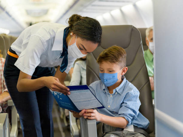 Flight attendant helping a boy in an airplane and both wearing a facemask Friendly flight attendant helping a boy in an airplane and both wearing a facemask - travel during the COVID-19 pandemic concepts crew stock pictures, royalty-free photos & images