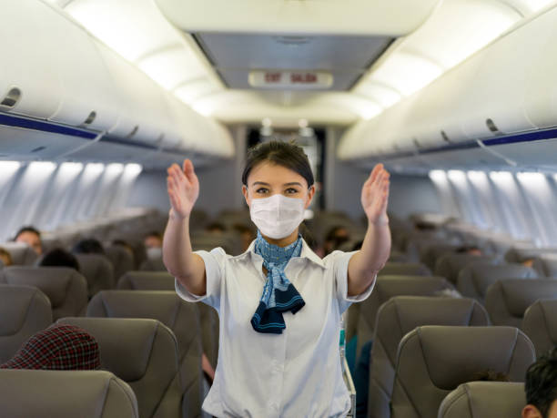 Flight attendant showing the emergency exit in an airplane wearing a facemask Portrait of a flight attendant showing the emergency exit in an airplane wearing a facemask before takeoff - traveling during the pandemic concepts crew stock pictures, royalty-free photos & images