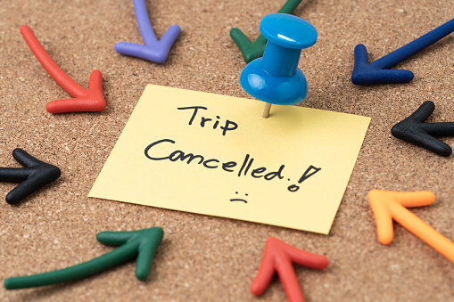 Flight cancelled due to COVID-19 virus spread outbreak, cancel plan to travel reminder concept, Thumbtack pushpin with multi arrows pointing to small paper note written the word Trip Cancelled