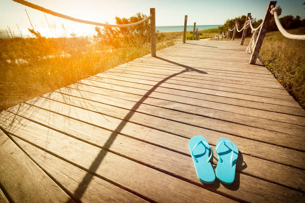 Flip flops on a wooden footpath to the beach on the dunes at sunset Horizontal view of blue flip flops left on a wooden footpath to the beach on the dunes at sunset. Copy space available for text and/or logo. DSRL outdoors photo taken with Canon EOS 5D Mk II and Canon EF 17-40mm f/4L IS USM Wide Angle Zoom Lens flip flop stock pictures, royalty-free photos & images