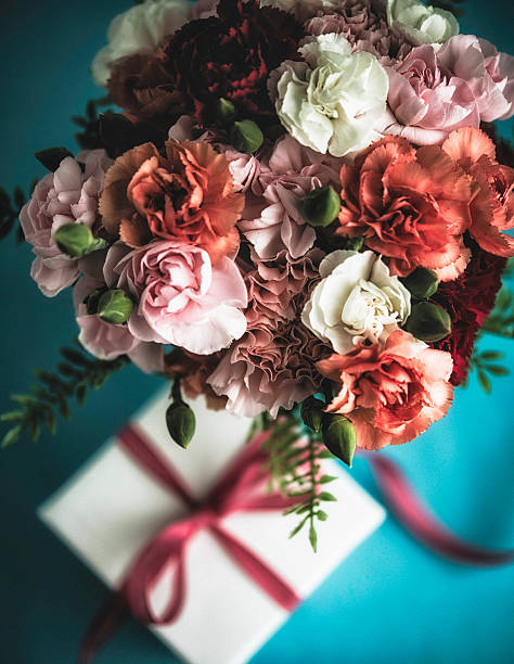 Układanie kwiatów z goździkami, paprocią i prezentem na specjalne okazje