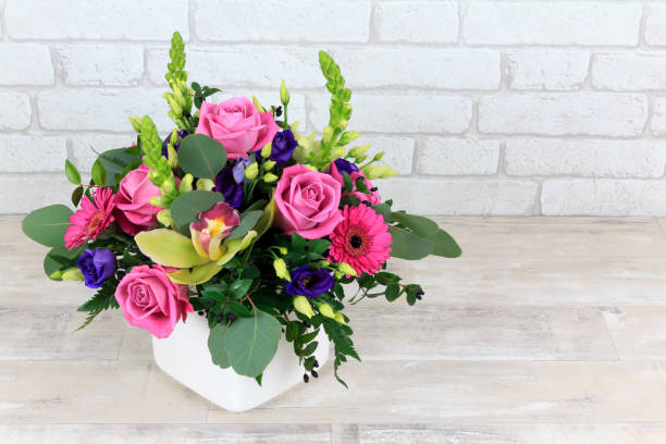 flowers Mixed pink floral arrangement in a white pot on shabby worktop with white brick background flower arrangement stock pictures, royalty-free photos & images