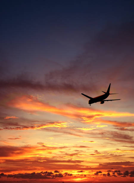 Flying commercial airplane over orange color dramatic sunset sky stock photo