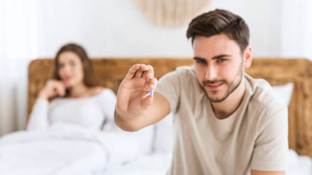Focus on blue pill in hands of happy young man, and smiling wife sits in bed in modern interior of bedroom Mens health and sexual problems, male power and libido. Focus on blue pill in hands of happy young man, blurred smiling wife sits in bed in modern interior of bedroom, close up, panorama, free space anti impotence tablet stock pictures, royalty-free photos & images