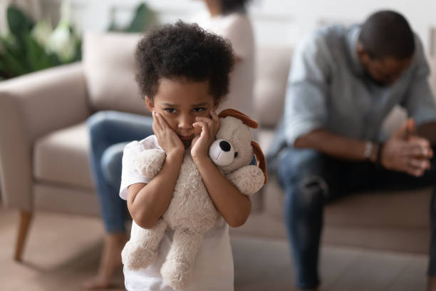 Focus on boy closed ears not to hear parents scandal On foreground close up focus on african lonely boy embraces soft toy as symbol seeking for protection support, son closed ears not to hear parents scandal, divorce negative affect to children concept couple divorce photos stock pictures, royalty-free photos & images