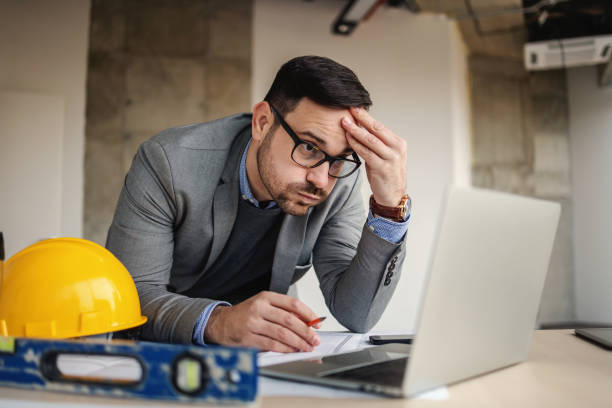 Focused architect holding his head, sights and looking at laptop. Something got wrong. stock photo