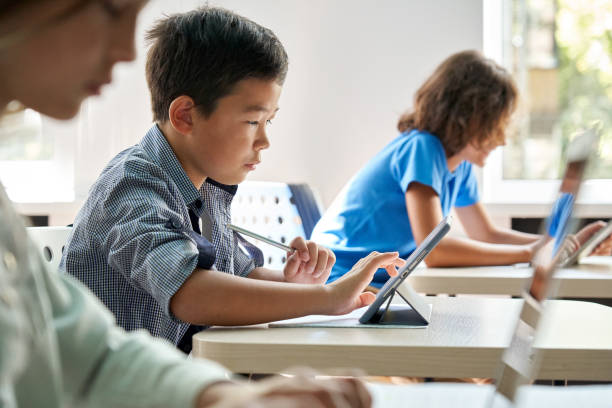 Focused Asian school boy using digital tablet at class in classroom. stock photo
